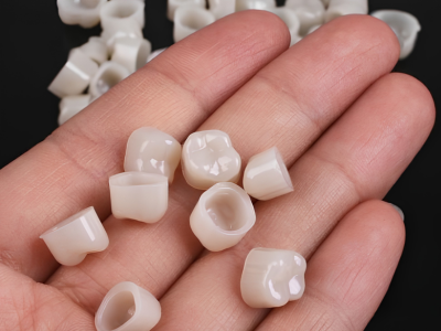 Close-up of a hand holding several small white dental ceramic crowns on a black background.