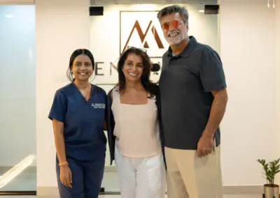 Three smiling colleagues posing together in a bright office lobby; two women in scrubs and a tall man wearing orange sunglasses, with a logo on the wall behind them.