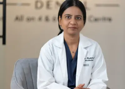 Female doctor in a white coat sits in a gray chair in a medical office, hands folded in her lap.